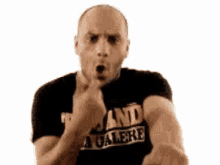 a bald man in a black shirt is making a funny face and pointing at the camera .