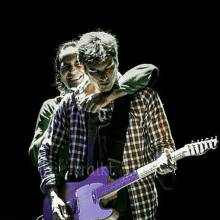 a man holding another man 's arm while playing a purple guitar with the word krakt written on the bottom