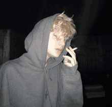 a young man wearing a hoodie is smoking a cigarette in the dark .