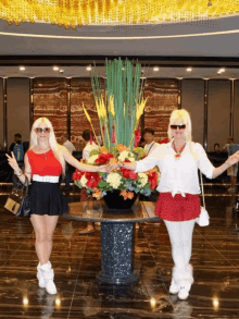 two women standing in front of a table with flowers in it