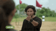 a man in a black shirt is pointing at a woman in a field with flags in the background .