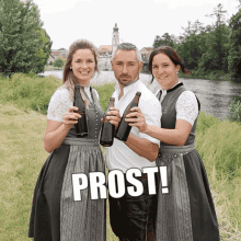 a man and two women holding beer bottles in front of a river and the word prost is above them