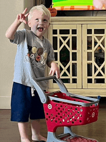 a young boy wearing a mickey mouse shirt is standing next to a target shopping cart