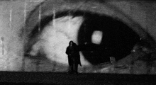 a black and white photo of a person standing in front of a large eye .