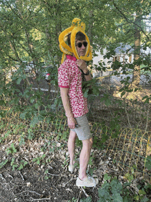 a man wearing a pink shirt and a yellow octopus hat is standing in the woods