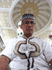 a man wearing glasses and a white shirt is sitting in a mosque