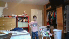 a boy in a pink shirt with a shark on it stands in a bedroom