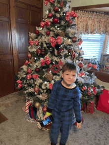 a young boy standing in front of a christmas tree holding a cell phone