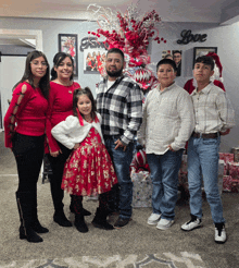 a family posing for a picture in front of a christmas tree with a love sign on the wall behind them