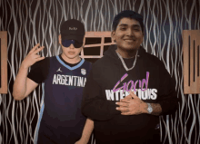 a man in an argentina jersey stands next to another man in a good intentions hoodie