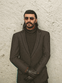 a man in a suit and sunglasses stands in front of a wall