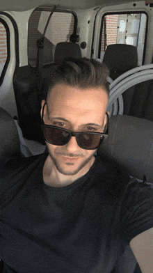 a man wearing sunglasses and a black shirt is sitting in the back seat of a car