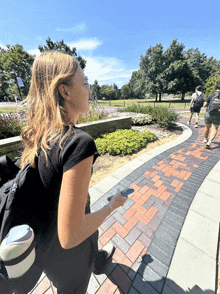 a woman walking down a sidewalk with a brick walkway and a sign that says ' a ' on it