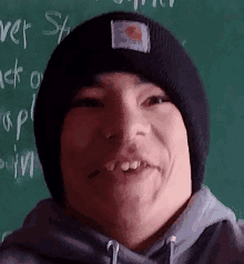 a man wearing a black carhartt beanie is smiling in front of a blackboard