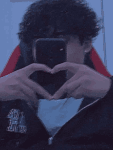 a man making a heart shape with his hands in front of his phone