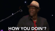 a man in a hat is playing a guitar and singing into a microphone while asking how you doin ' .