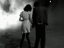 a black and white photo of a man and woman holding hands .