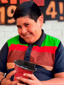 a boy is holding a cup of coffee in front of a sign that says 19 4