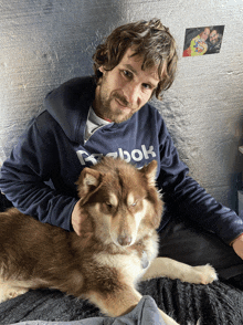 a man wearing a blue reebok sweatshirt holds a brown dog