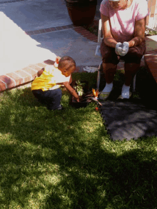 a woman in a pink shirt sits on a chair while a little boy in a yellow shirt plays in the grass