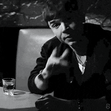 a black and white photo of a man sitting at a table with a glass of water in front of him .