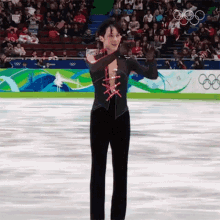 a man in a black and red outfit is standing on a ice rink with the olympic rings in the background