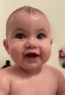 a baby with long eyelashes is smiling in the bathtub