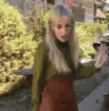 a woman in a green turtleneck and red skirt is standing on a sidewalk .