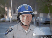 a police officer wearing a blue helmet is smiling while standing on a street .