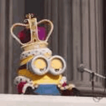 a minion is wearing a crown and sitting at a podium .