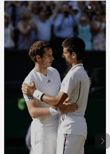 two men are hugging each other on a tennis court and one has the word adidas on his shirt