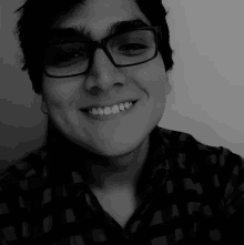 a young man wearing glasses and a plaid shirt smiles in a black and white photo