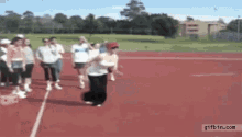 a group of people are walking on a red track and one of them is jumping in the air .