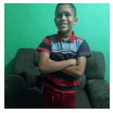 a young boy is standing with his arms crossed in front of a couch .