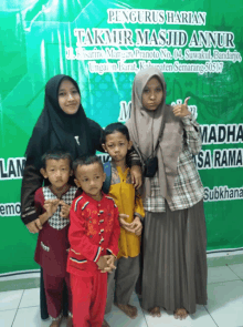 a group of children are posing for a picture in front of a sign that says " pengusharian takmir masjid annup "