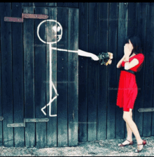 a woman in a red dress is standing in front of a wooden wall with a stick figure drawing on it