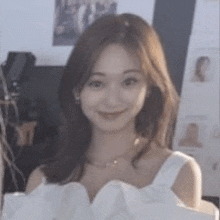 a close up of a woman wearing a white dress and a necklace smiling .