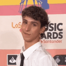 a young man in a white shirt and tie stands in front of a sign that says los music awards santander