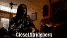 a man with long hair is sitting at a table with the name giesel stridelberg written on the bottom