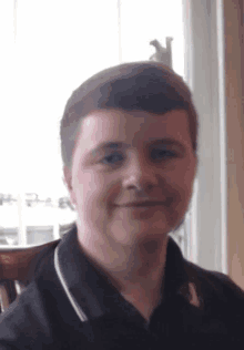 a young man wearing a black shirt with a white collar smiles for the camera