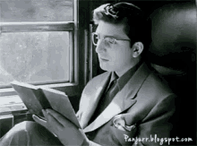 a man in a suit and tie is reading a book while sitting on a train .