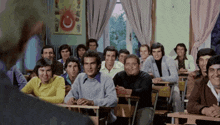 a group of men sit at desks in a classroom with a turkish flag hanging on the wall behind them