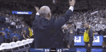 a man in a suit stands in front of a crowd at a basketball game between florida and uconn .