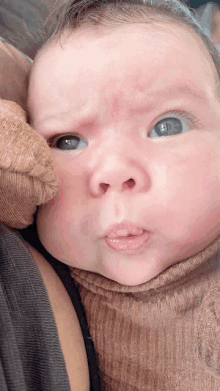 a close up of a baby 's face with a brown sweater on