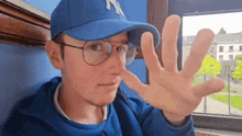 a man wearing a blue hat and glasses is making a stop gesture with his hand .