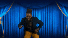 a man with a beard is dancing on a stage with blue curtains behind him