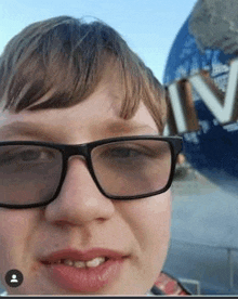 a young boy wearing glasses is taking a selfie in front of the universal studios globe .