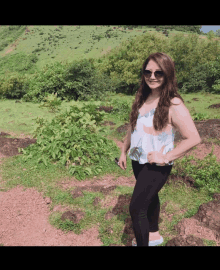 a woman in a white top and black pants stands in a field