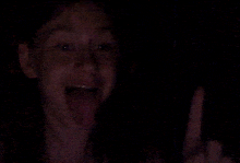 a person is making a funny face in the dark and giving the middle finger .