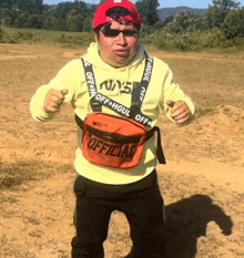 a man wearing a yellow hoodie and a red hat is holding an orange fanny pack that says official on it